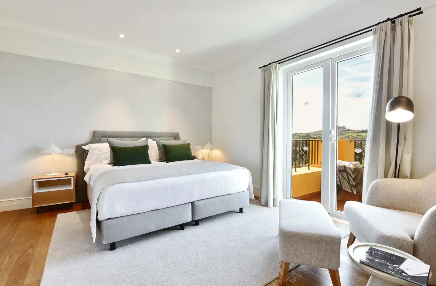 Geräumiges Schlafzimmer im Hotel mit einem großen Bett, Sitzecke und Blick auf den Balkon, ideal für einen erholsamen Urlaub.