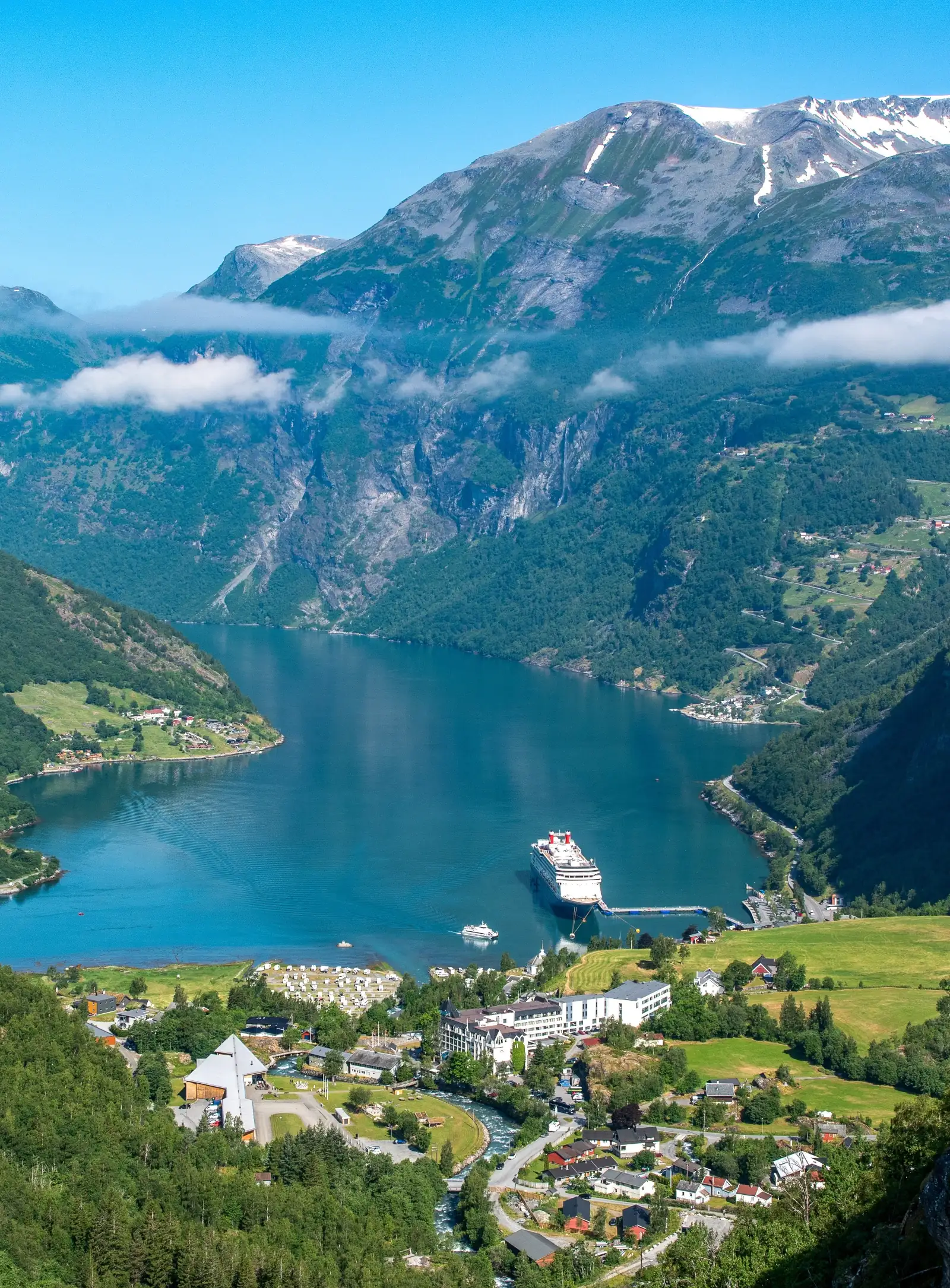 Fjordlandschaft Norwegens, mit einem Kreuzfahrtschiff im Wasser, umgeben von Bergen und grünen Hügeln.
