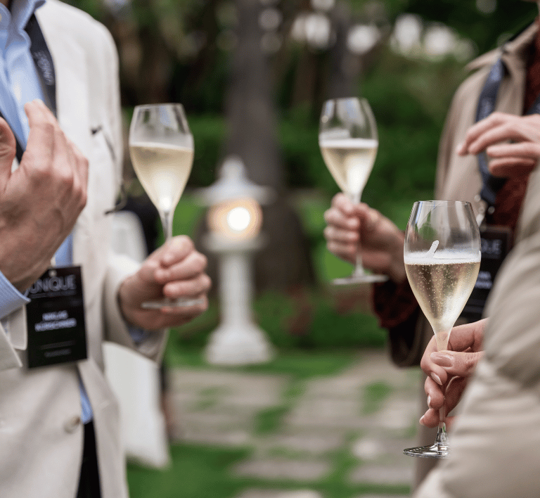 Geselliges Anstoßen mit Freunden bei einer eleganten Veranstaltung im Freien Eine Gruppe von Personen stoßt mit Sektgläsern an und genießt eine elegante Outdoor-Veranstaltung in einer schönen Gartenanlage.