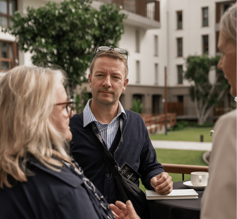 Gespräch beim Networking-Event im Garten des modernen Hotels Zwei Personen im Gespräch auf einer Terrasse eines modernen Hotels, umgeben von Grün, beim Networking-Event in der Region.