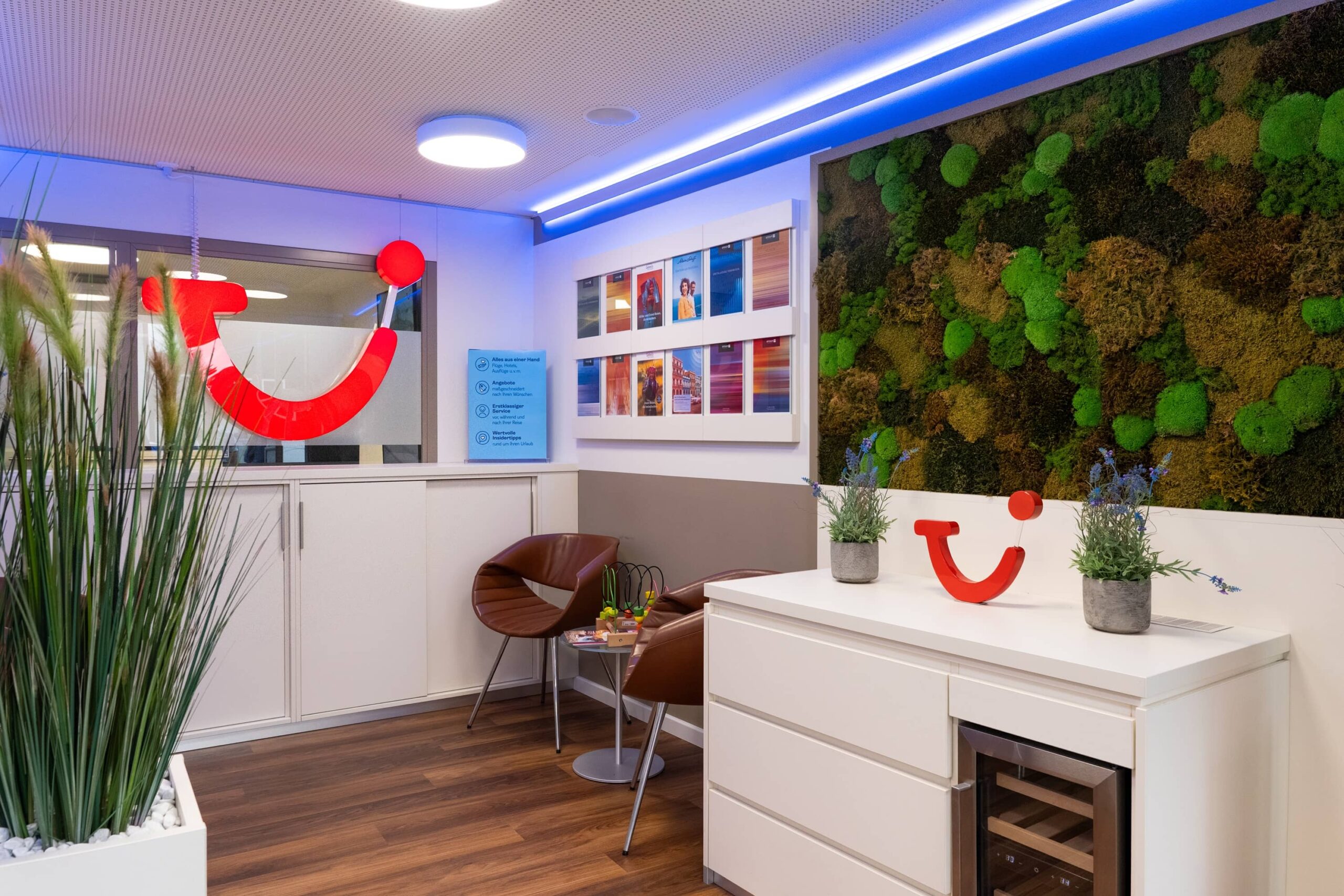 Moderne Empfangslounge im TUI Reisebüro mit stilvollem Design und freundlicher Atmosphäre Empfangslounge im TUI Reisebüro mit modernem Design, grünen Pflanzen und farbenfrohen Reisefotos, ideal für Reisebuchungen.